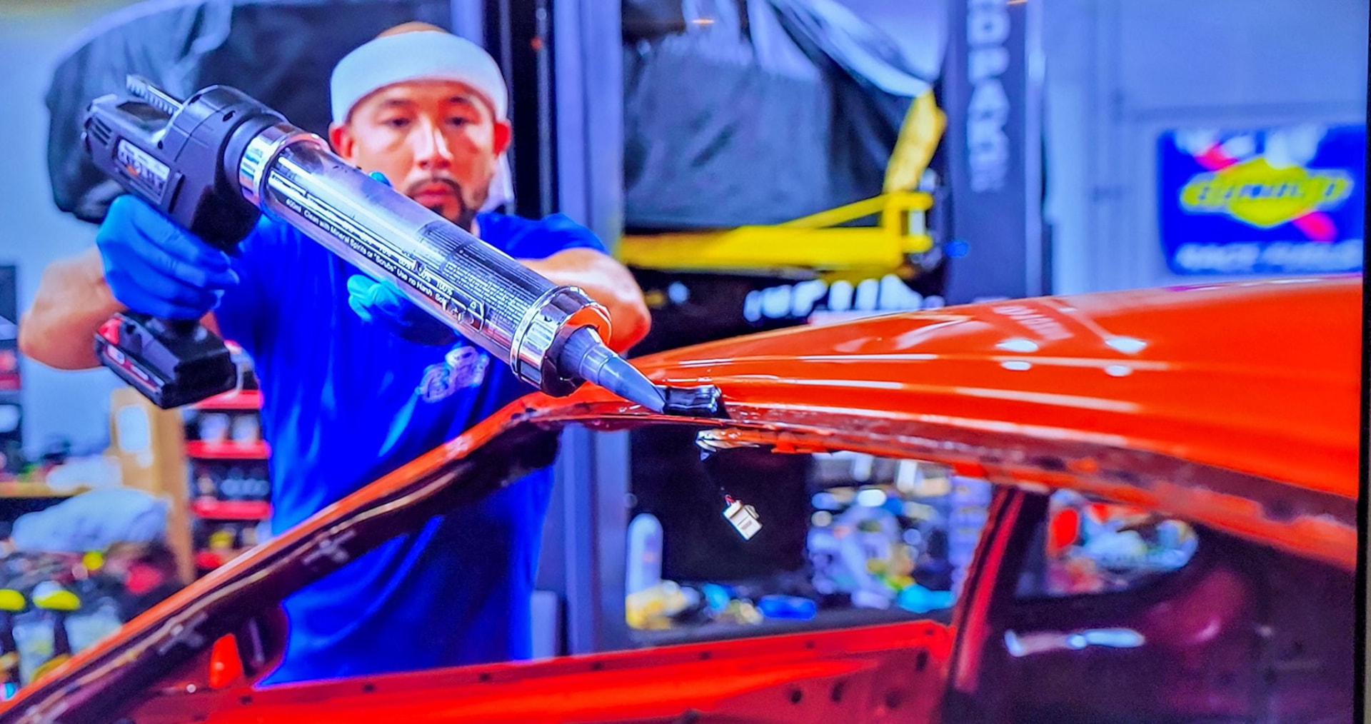 Technician applying windshield adhesive to a red car in the shop